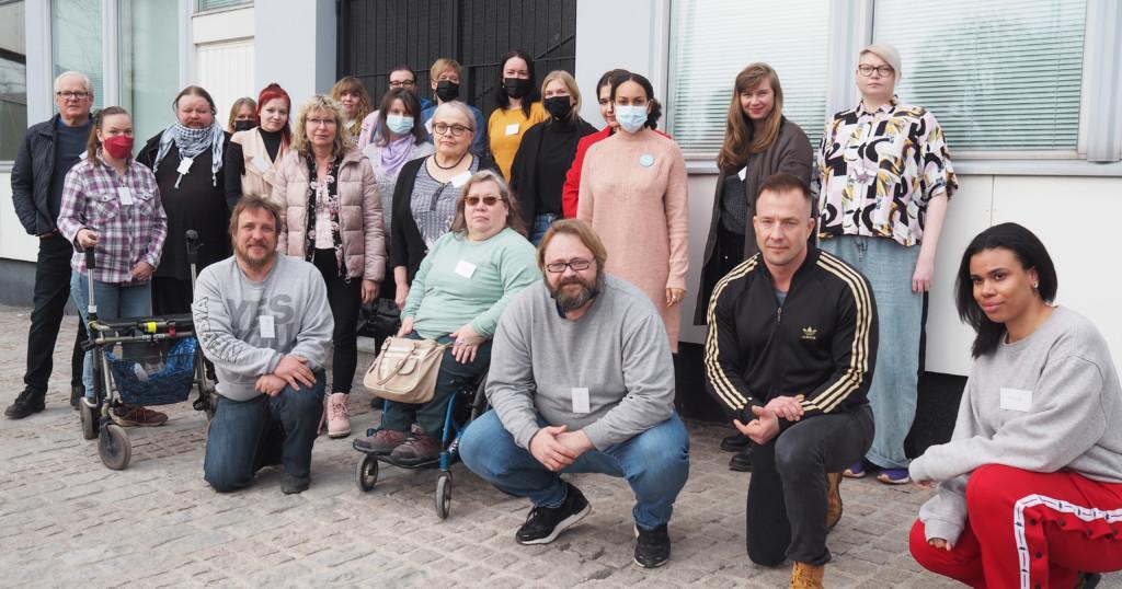 Ihmisoikeusliiton 20-henkinen vaikuttajaryhmä yhteiskuvassa harmaasävyisen rakennuksen edessä.